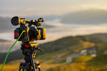 Modern video camera filming on a tripod a beautiful morning panorama. Typical work for a videographer in the morning, handheld camera with signal cable in the backの写真素材