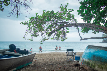 Local people are taking a swim in a sea in costa rica, view from the beach, looking between two boats and some trees. Back view of people.の写真素材