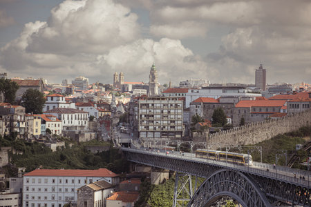 Tram of porto is moving over the famous metal bridge over douro river, with cityscape of porto in the background. Cloudy dayの写真素材
