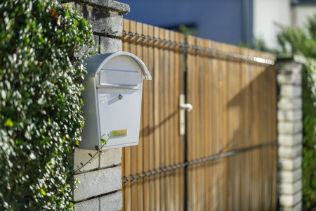 White metal letterbox or letter box mounted on a brick wall next to a wooden house entrance. Night time setting. Closed lid for lettersの写真素材