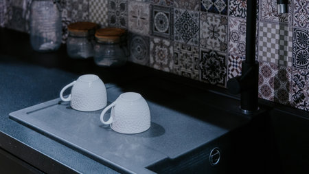 Two white upside down cups drying next to a sink in modern clean kitchen. Counter with cute tiles.の写真素材