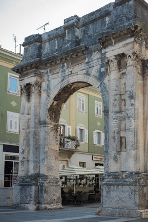 Old roman gate in pula, croatia. Massive old city entrance or arc in the town square. Other houses aroundの写真素材