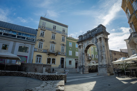 Old roman gate in pula, croatia. Massive old city entrance or arc in the town square. Other houses aroundの写真素材