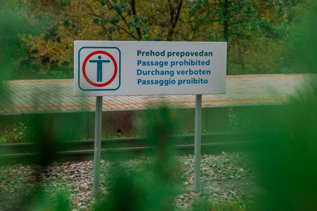 Sign board for prohibitinhg crossing of train tracks on a station, written in multiple languages such as slovenian, english, german and italianの写真素材