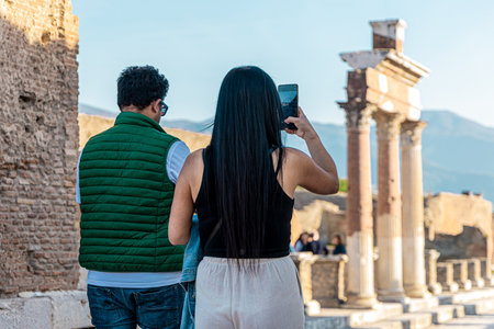 Back view of an unknown couple taking photos at Pompei archeological site close to Naples, Italy. Beautiful sunny day to visit the ruinsの写真素材