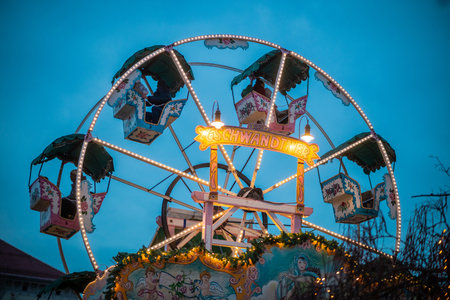 Big carnival ferris wheel is turning around in christmas spirit. Visible christmas lights, blue sky, dusk ambient, romantic. Looking through the lightsの写真素材