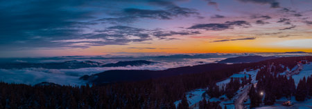 Epic drone panorama of Rogla ski resort in Pohorje region of Slovenia. Visible colorful sunset, clouds in the valley and small hills piercing through the clouds.の写真素材