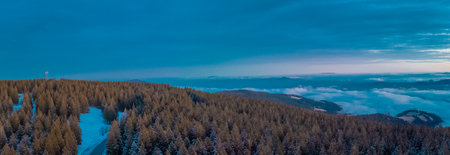 Epic drone panorama of Rogla ski resort in Pohorje region of Slovenia. Visible colorful sunset, clouds in the valley and small hills piercing through the clouds.の写真素材