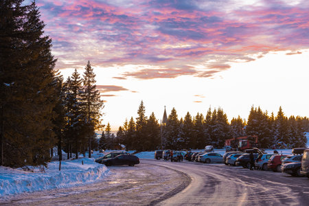 Cars parked on the parking spot on top of Rogla ski resort, visible winding road, cars and epic romantic sunset in winter.の写真素材