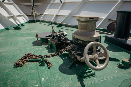 Winch with a chain for an anchor on a steel ship. Visible command wheel and front part of the ship.の写真素材