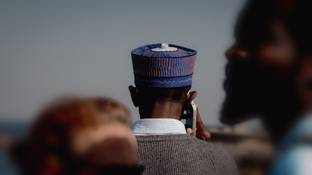 Unknown african man is talking on the mobile phone facing away from the camera. Man caught talking between two other unknown peopleの写真素材
