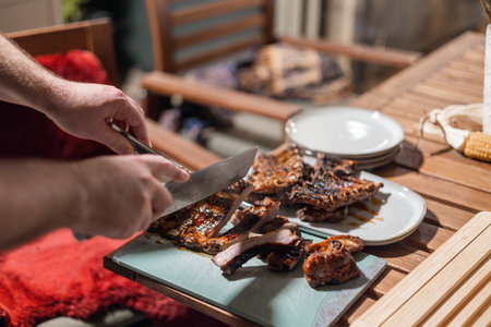 Unknoiwn man is seen cutting ribs from the grill using a sharp knife and a forkの写真素材