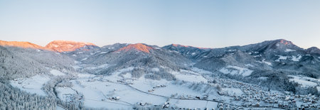 Beautiful panorama of village of Ljubno ob Savinji in cold winter morning. Visible haze from the river, sun rising up and smoke coming out of smokestacks.の写真素材