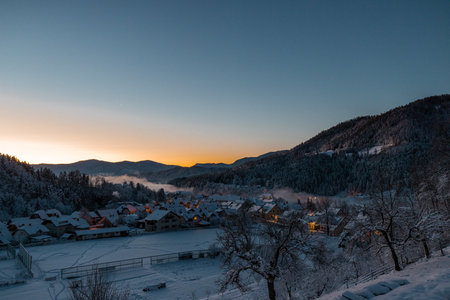 Beautiful village of Ljubno ob Savinji in cold winter morning. Visible haze from the river, sun rising upの写真素材