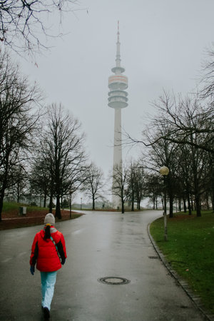 Radio tower or tv tower in munich or munchen, rising high up, viewed from the park in dull gray weather. Pedestrian walking towards it.の写真素材