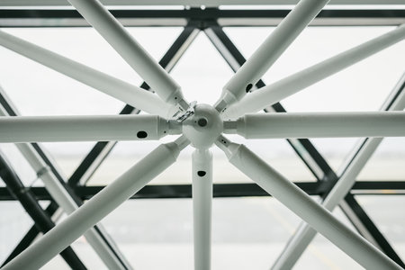 Contemporary roof construction for a modern building such as airport. Visible metal poles coming from central round joint. Glass windows in the backの写真素材