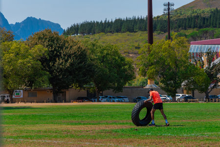 Man training with an old tractor tire on a stadium in Stellenbosch, south africa. Person using a tyre as a weight and weight training, sunny day.の写真素材