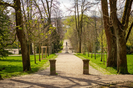 A gravel path in Tivoli Park, Ljubljana, lined with bare trees and green grass, leads to a statue on...