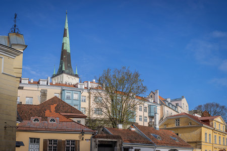 A bright spring day in Tallinn, Estonia, showing charming pastel buildings and the tall spire of St. Olaf s Church rising above the historic rooftops under a vivid blue sky.の写真素材