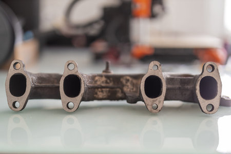 A rusty cast iron exhaust manifold with freshly machined, straightened port faces, lying on a glossy...