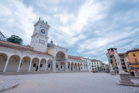 Iconic Piazza della Libert in Udine, Italy, showcasing Loggia del Lionello and Clock Tower. Features Venetian Gothic architecture, arches, stairs, and a lively square under a cloudy sky.の写真素材