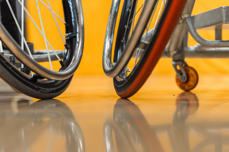 a close-up of wheelchair basketball players on an indoor court. Two chairs with wheels and parts in focus against a blurred background of the gym floor and walls.の写真素材