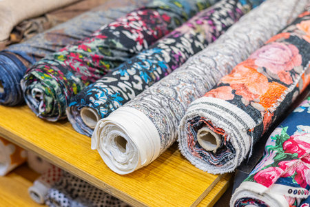 Close-up of rolled fabrics on a wooden shelf, featuring intricate houndstooth in red, black, green,...