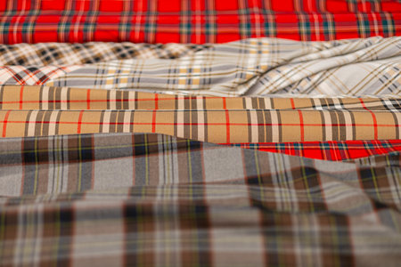 Close-up of stacked plaid fabric rolls in tartan patterns, featuring bold red, beige, gray, and multicolored checks. Textures vary from crisp to soft, with foreground slightly blurred.の写真素材