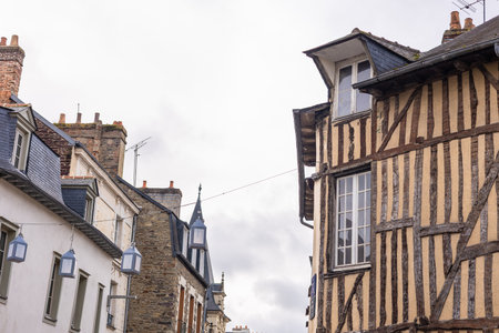 A narrow street in Rennes lined with historic half-timbered houses and stone buildings. The weathered wooden beams and slate roofs show the city s medieval charm under a soft, cloudy sky.の写真素材
