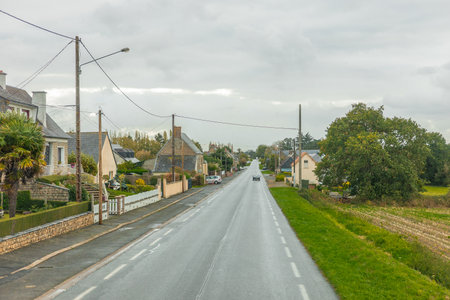 A quiet rural road lined with houses and gardens in a small French village on a cloudy day, showing calm countryside life and traditional architecture.の写真素材
