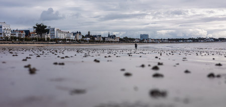 Panoramic shot of Royan Beach features a wide expanse of sand and calm water under a dramatic sky filled with scattered clouds. Modern buildings line the distant shore.の写真素材
