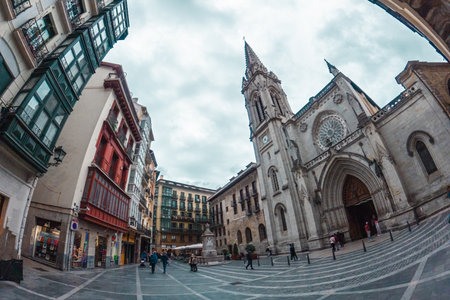 A fisheye lens captures Bilbaos Plaza Nueva, with its historic architecture, bustling square, and the prominent Santiago Cathedral under a dramatic sky.の写真素材