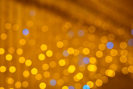 Abstract, dreamy background texture featuring soft, round bokeh lights in warm golden and amber tones, accented by subtle, contrasting points of blue light.の写真素材