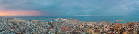 Bari at dusk with a panoramic view of the historic center, bustling port, and calm Adriatic Sea under dramatic clouds and soft sunset light.の写真素材