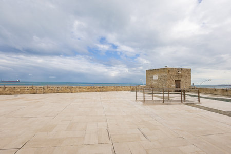 The expansive limestone terrace of the Fortino di SantAntonio in Bari stretches toward the Adriatic Sea. A historic stone guardhouse stands under a dramatic cloudy sky, overlooking the coastline.の写真素材