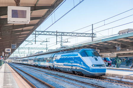 A sleek blue Intercity train stands at the platform in Bari Centrale station, Italy. The sunny railway scene features overhead lines, metal station canopies, and carriages waiting for passengers.の写真素材