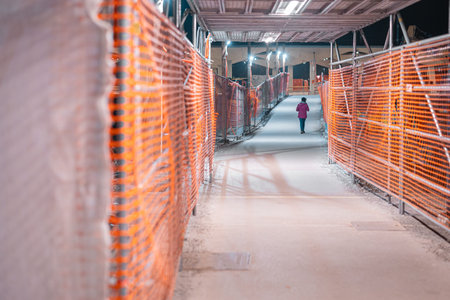 Night pedestrian corridor at Ljubljana train station renovation: temporary walkway lined with orange...