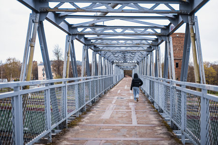 A metal pedestrian overpass spans multiple railway tracks in Narva, Estonia. The bridge features a...