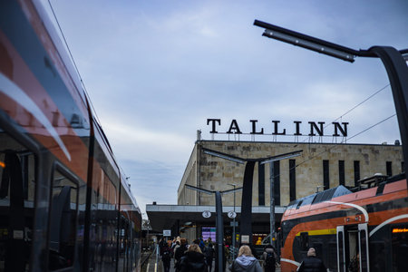 A view of the Balti Jaam railway station in Tallinn, Estonia. Modern orange trains flank a platform crowded with commuters under an overcast sky, with a large "TALLINN" sign atop the station.の写真素材