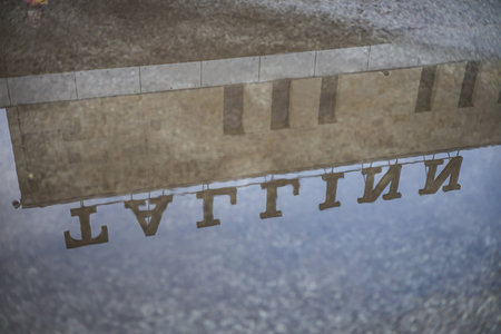 An artistic, inverted reflection of the "TALLINN" station sign and stone building visible in a puddle on the ground, capturing a moody, rainy-day perspective of the Balti Jaam railway hub.の写真素材
