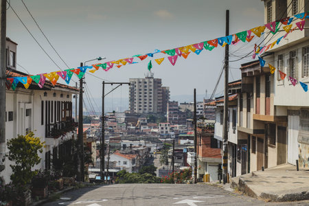 Festive colorful banners stretch across a steep street in Cali, Colombia, framing a downhill view of the city s dense urban landscape and distant hills under a bright, hazy sky.の写真素材