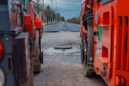 Framed by the orange wheels of heavy rollers, the view looks down the newly paved road in Siska,...