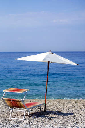 Recliner and umbrella on a pebble beach.の写真素材