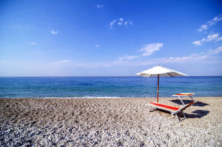 Recliner and umbrella on a pebble beach.の写真素材