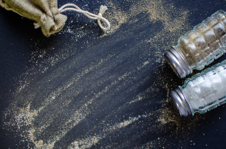 Culinary Duo: Salt and Pepper with Burlap Sack on a Dark Surfaceの写真素材