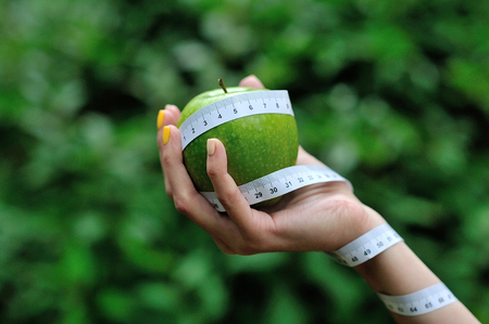 Female hand with green apple and measuring tape.の写真素材
