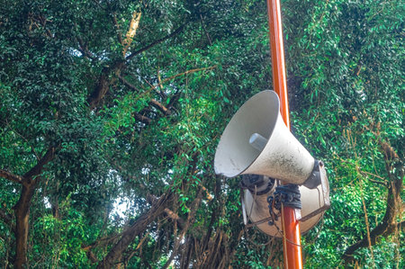 a loudspeaker attached to an iron pole with a backdrop of shady treesの写真素材