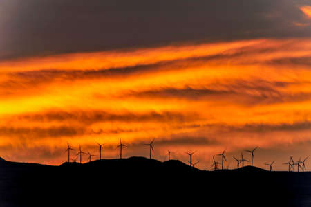 Sunset over the mountains planted with electric wind turbinesの写真素材