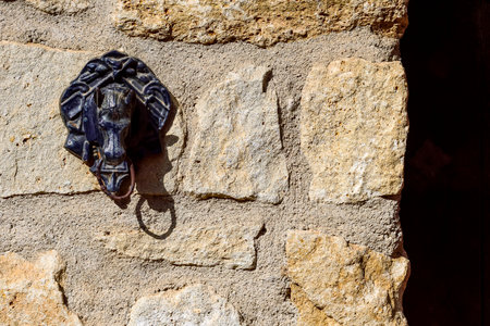 A close-up of an ornate elephant-shaped door knocker on a textured stone wall, shadow play.の写真素材