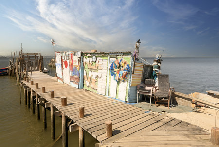 A weathered wooden pier and small hut extend into a tranquil river, with a lone boat anchored nearby.の写真素材